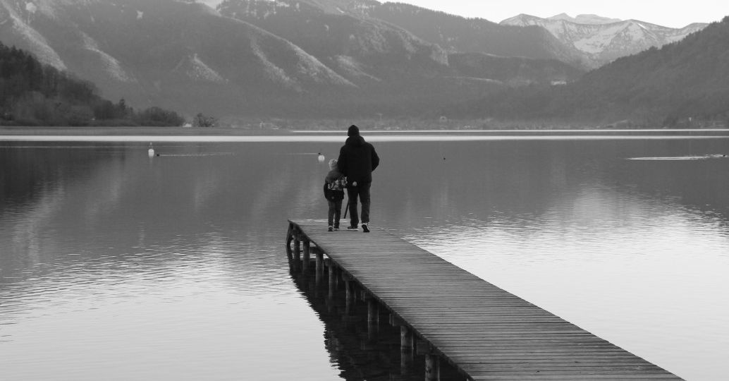 black-and-white-shot-of-father-and-son-silhouettes-in-front-of-lake-and-mountain-view_t20_ompxjQ