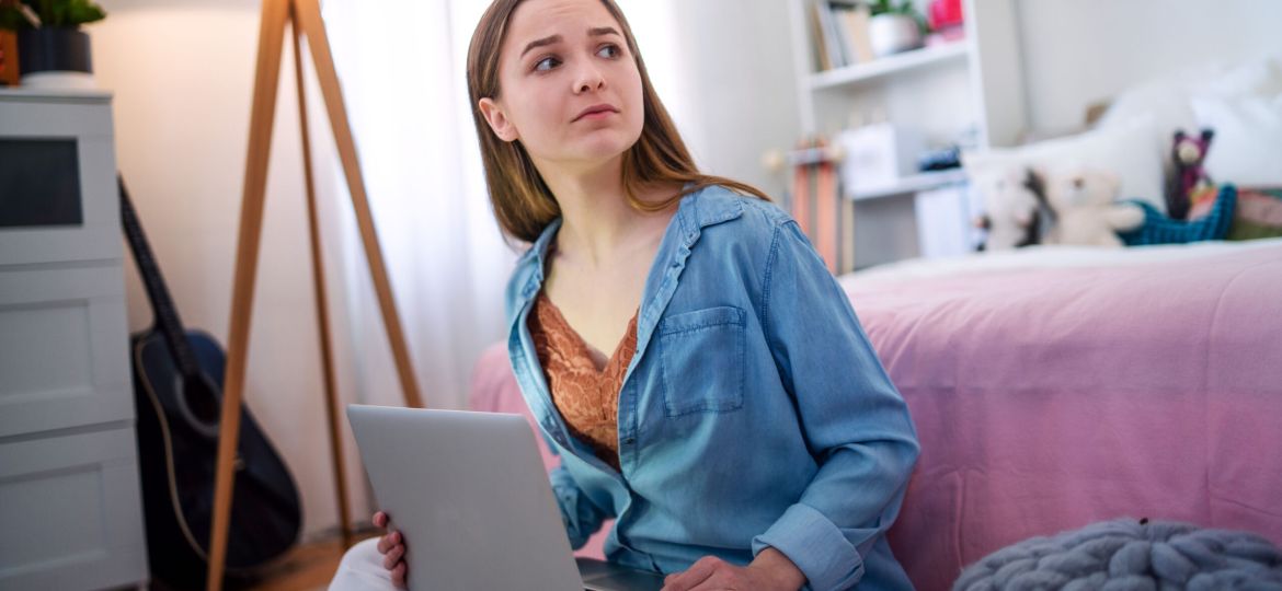 Sad and worried young girl with laptop sitting indoors, internet abuse concept.