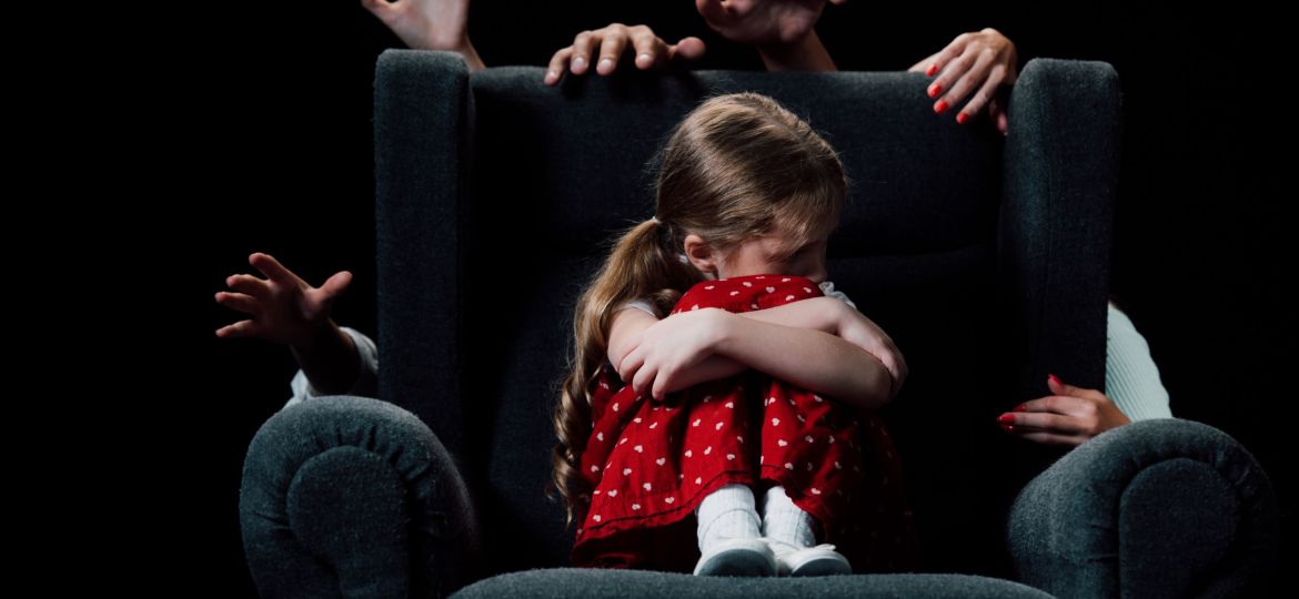 scared child sitting in armchair surrounded with human hands isolated on black